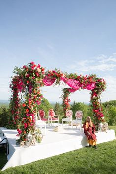 a man sitting on top of a lush green field under a pink flower covered arch