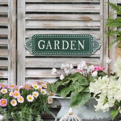 a garden sign sitting on the side of a building next to potted plants and flowers