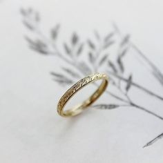 a gold wedding ring sitting on top of a piece of paper with leaves in the background