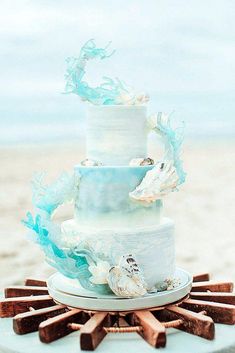 a three tiered cake with blue and white icing on a table at the beach