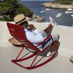 a man sitting in a red rocking chair on top of a roof next to the ocean