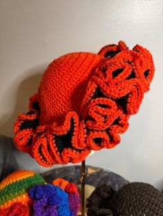 an orange crocheted hat sitting on top of a wooden stand next to other knitted hats