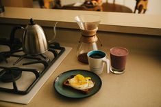 a plate with an egg on it next to a cup of coffee and a kettle