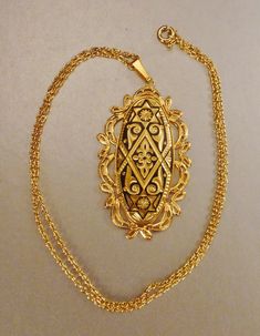 A vintage damascene large oblong pendant, a golden floral and geometric designs framed by intricate gold tone filigree border, oxidized black on 24 karat gold plate as you can see from the pictures. It is in great vintage condition as seen in photos It measures 2 by 1 1/4 in wide wot5h am 18 in gold tone chain as seen in photo. A lovely damascene decorative large pendant addition to your collection, a welcome birthday or Mother's DAY gift! Gold Rectangular Filigree Jewelry, Antique Gold Necklace With Rectangular Pendant, Ornate Rectangular Gold Jewelry, Ornate Gold Rectangular Jewelry, Victorian Gold Rectangular Necklace, Victorian Rectangular Gold Necklace, Gold Rectangular Jewelry With Intricate Design, Rectangular Gold Jewelry With Intricate Design, Vintage Gold Filigree Necklace