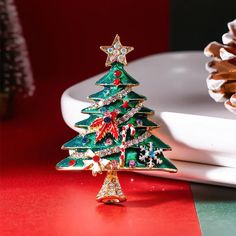 a christmas tree brooch sitting on top of a red table next to a white plate