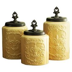 three yellow canisters with black lids on white background, one has an ornate design