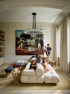 a group of people sitting on top of a white couch in a living room next to a painting