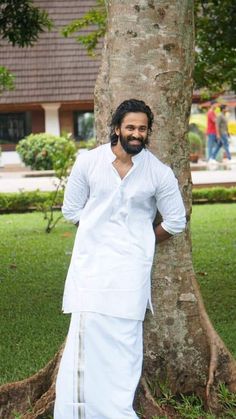 a man standing in front of a tree wearing a white outfit and holding his hands on his hips