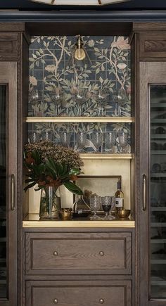 a wooden cabinet with glass doors and shelves filled with wine glasses, vases and flowers