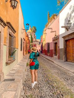 a woman walking down a cobblestone street in an old town with colorful buildings