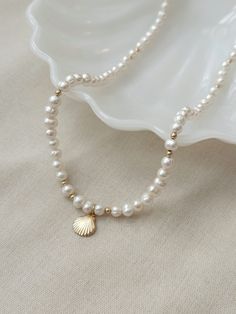 This genuine baroque Pearl necklace is the perfect accessory to elevate your summer look! This stunning necklace is crafted with off round irregular pearls and features a beautiful 14K Gold Filled or 925 Silver scallop shell charm. It's the perfect addition to your jewelry collection and is sure to become a beachy ocean inspired wardrobe staple.  * 14K Gold Filled or 925 Sterling Silver accents * Adjustable 18" - 20" length * 10mm 14K Gold Filled or 925 Sterling Silver Scallop Shell charm * Natu Elegant Shell-shaped Pearl Drop Necklace, Delicate Baroque Pearl Necklace With Round Beads, Beaded Necklace With Baroque Pearl And Pearl Charm, Beaded Necklace With Baroque Pearl Charm, Elegant Shell Necklace With Baroque Pearl Drop, Baroque Pearl Necklace With Pearl Charm, Elegant Gold Shell Necklace With Round Beads, Pearl White Beaded Baroque Pearl Necklace, Elegant Pearl Shell Necklace With Round Beads