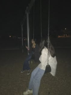 two people sitting on swings in the dark