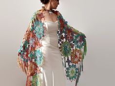 a woman in a white dress is wearing a colorful crochet shawl with flowers on it