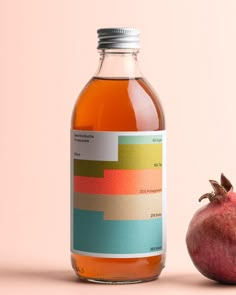 a bottle of apple cider next to a pomegranate on a pink background