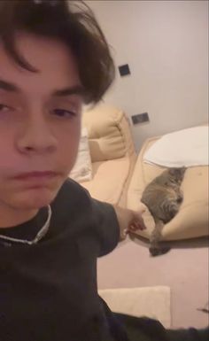 a young man sitting on top of a couch next to a gray and white cat