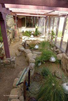 the inside of a building with plants and rocks on the ground in front of it