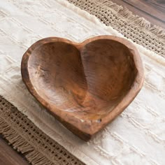 a wooden heart shaped bowl sitting on top of a white tablecloth next to a rug