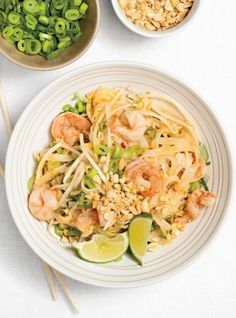 a white plate topped with noodles and shrimp next to bowls of green beans, limes and rice