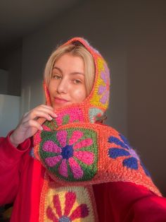 a woman in a red jacket is holding up a crocheted object