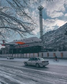 a white car driving down a snow covered road next to a tall building with an orange roof