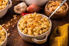 three bowls filled with macaroni and cheese on top of a wooden table next to garlic