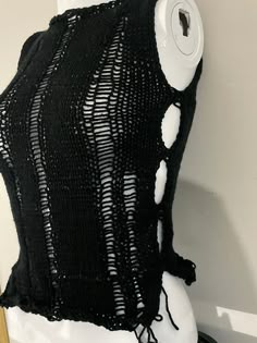 a black knitted vest with holes on the front and back, attached to a white mannequin's head