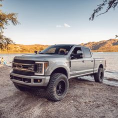 a silver truck parked on top of a sandy beach next to the ocean with people swimming in the water