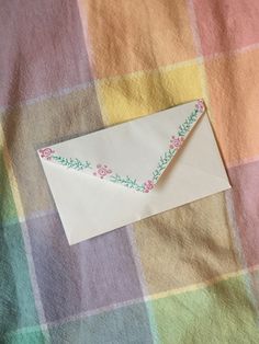 an envelope is laying on a checkered blanket with a flowered border and paper sticking out of it