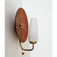 a wall mounted light with a white glass shade on it's arm and gold fittings