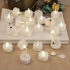 several white candles sitting on top of a book next to some flowers and other items