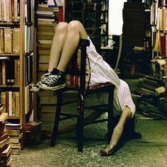 a person sitting in a chair with their legs up on a book shelf full of books