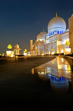 a large white building lit up at night with its lights on and reflecting in the water