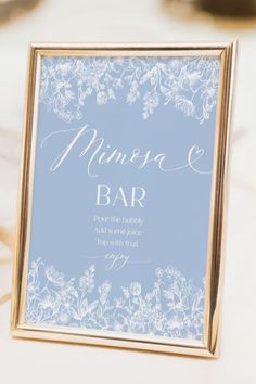 a close up of a sign on a table with flowers in the background and gold frame