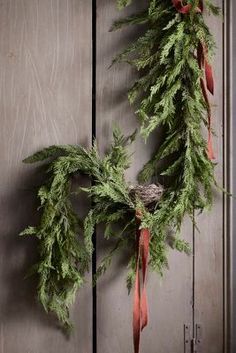 a wreath hanging from the side of a wooden door with red ribbon around it's edges