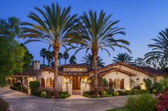 a home with palm trees and landscaping in front of it at dusk, surrounded by greenery