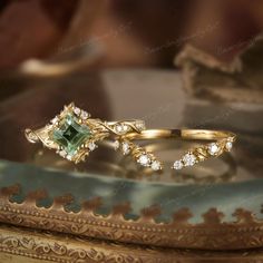 two gold rings with green and white stones on them sitting on top of a table