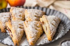 several pastries are on a plate with apples in the backgroung and powdered sugar