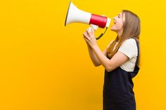 a woman holding a red and white megaphone in front of her face on a yellow background