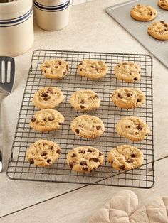 chocolate chip cookies cooling on a wire rack next to baking utensils and cookie pans