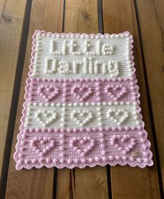 a pink and white crochet baby blanket on a wooden floor with the words little sister written across it