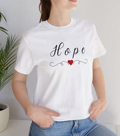 "This \"HOPE\" T-shirt is a classic unisex jersey short-sleeve tee. It reminds us to have Hope in all things. It is made of soft cotton and quality print. These t-shirts have ribbed knit collars to bolster shaping.  .: 100% Airlume combed and ringspun cotton  .: Tear away label Thank you for visiting the - \"Think Happy With Tammy Shop\" Here is a link to another product of ours in the Forgiveness theme that you might like.  https://www.etsy.com/listing/1486791636/christian-forgiveness-mugs-coff Pre-shrunk White Print Crew Neck T-shirt, White Letter Print T-shirt As Gift, Graphic Tee Crew Neck T-shirt As Gift, Graphic Tee Crew Neck As Gift, Graphic Tee With Crew Neck As Gift, Short Sleeve Tops With Text Print For Gift, Gift Crew Neck T-shirt With Custom Print, Short Sleeve T-shirt With Letter Print, White Letter Print T-shirt As A Gift