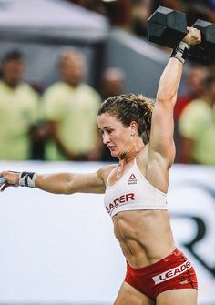 a woman holding two black dumbs while standing on top of a field