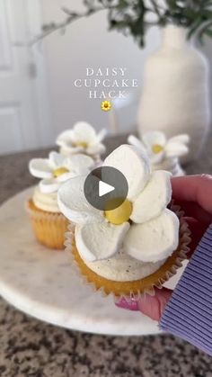 a person is holding a cupcake with white flowers on top and blue ribbon around it