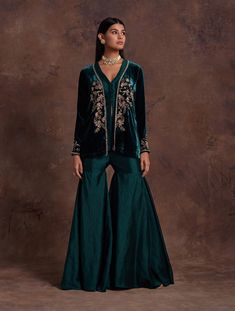 Editors Note Drape yourself in elegance with a green silk velvet jacket featuring hand embroidery at the front center and sleeves. Paired seamlessly with a silk peplum adorned with a V-neckline and potli buttons, along with complementing sharara pants, this ensemble exudes sophistication and style. Perfect for occasions where you seek a perfect balance of traditional craftsmanship and contemporary flair. Festive Velvet Saree Set, Velvet Sharara For Party And Festivals, Velvet Anarkali Sharara For Party, Elegant Velvet Palazzo Set For Wedding, Designer Velvet Traditional Wear With Long Sleeves, Festive Velvet Sharara With Traditional Drape, Elegant Velvet Palazzo Set With Zari Work, Velvet Anarkali Party Sets, Elegant Velvet Sharara For Festivals