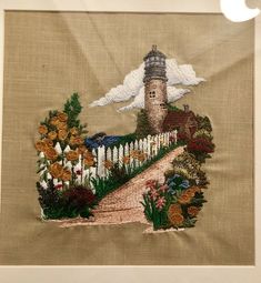 an embroidered wall hanging with flowers and a lighthouse