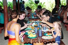 a group of people sitting around a wooden table eating food and drinking water at the same time