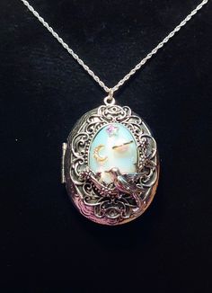 Here is a beautiful silver tone oval locket with a moonstone translucent stone in the center. The main colors of this necklace are silver and white. There are celestial bodies adhered to the moonstone. There is a gold metal moon with tiny rhinestones, a gold ringed (real opal) planet, and a iridescent Swarovski crystal star. There is silver filigree all around the moonstone. At the top and bottom of the filigree is two all seeing, all knowing eyes. There is also a bird on a branch at the bottom of the filigree. This locket is rather large. It is 2 Inches tall. It is 1 and 3/4 wide in the middle. It is approx. 1 and 2/8 tall by 1 inch wide inside oval dimensions for your photographs. You can put two pictures inside,one on the left and one on the right. Includes is a 16 Inch .925 Sterling Si Silver Celestial Oval Jewelry, Sterling Silver Oval Locket Necklace, Nickel-free, Oval Sterling Silver Nickel-free Locket Necklace, Oval Sterling Silver Locket Necklace Nickel Free, Celestial Silver Oval Pendant Jewelry, Nickel-free Silver Oval Locket Necklace, Silver Oval Locket Necklace Nickel-free, Silver Oval Locket Necklace Nickel Free, Silver Oval Locket Necklace With Adjustable Chain