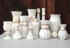 many white vases are lined up on a table with ribbons and bows around them