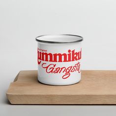 a white and red enamel mug sitting on top of a wooden tray with the words gummika & gangster printed on it