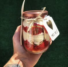 a hand holding a mason jar filled with red and white jello, topped with a heart tag